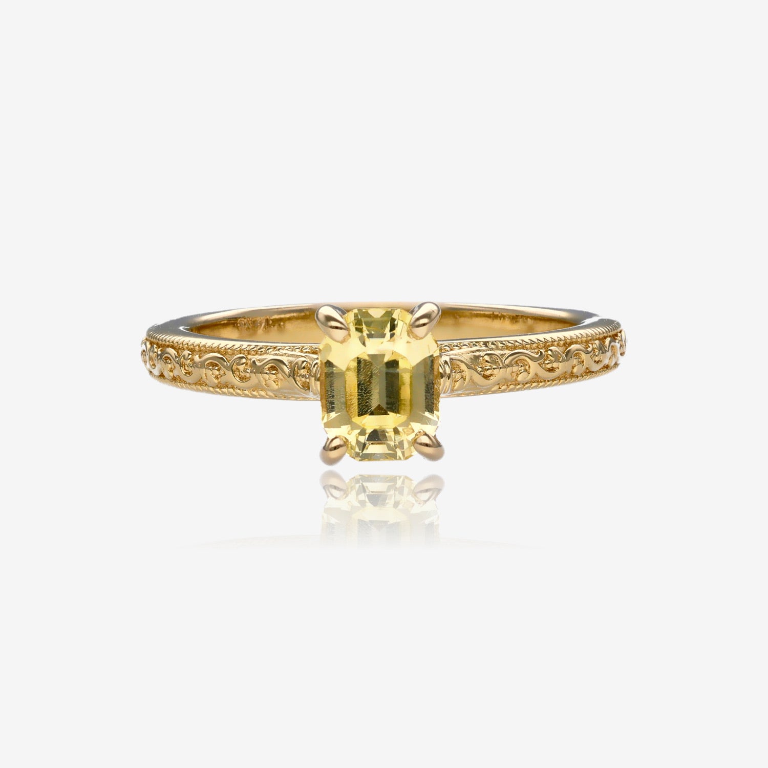 Yellow gold engagement ring with vintage detailing and emerald cut sapphire in a pale lemon yellow. Stone is set with four prongs, band measures approximately 2 mm thick.