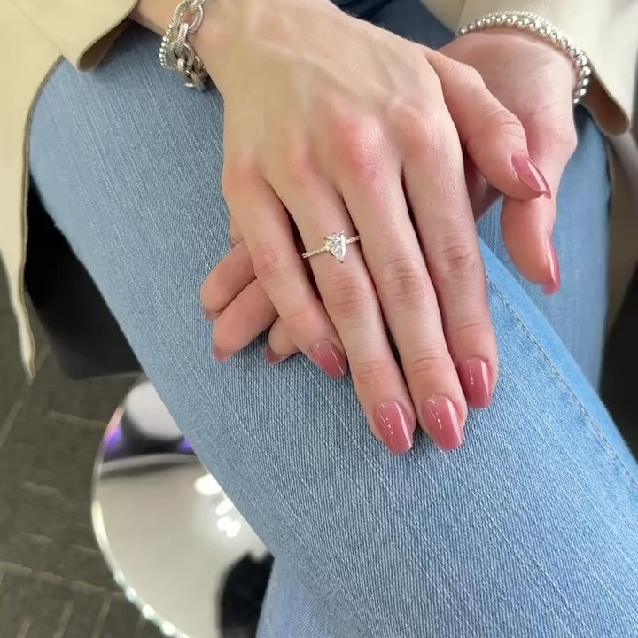 Woman’s hand showing a yellow gold ring with pear shape diamond center. Slender band is set with small diamonds all down the side
