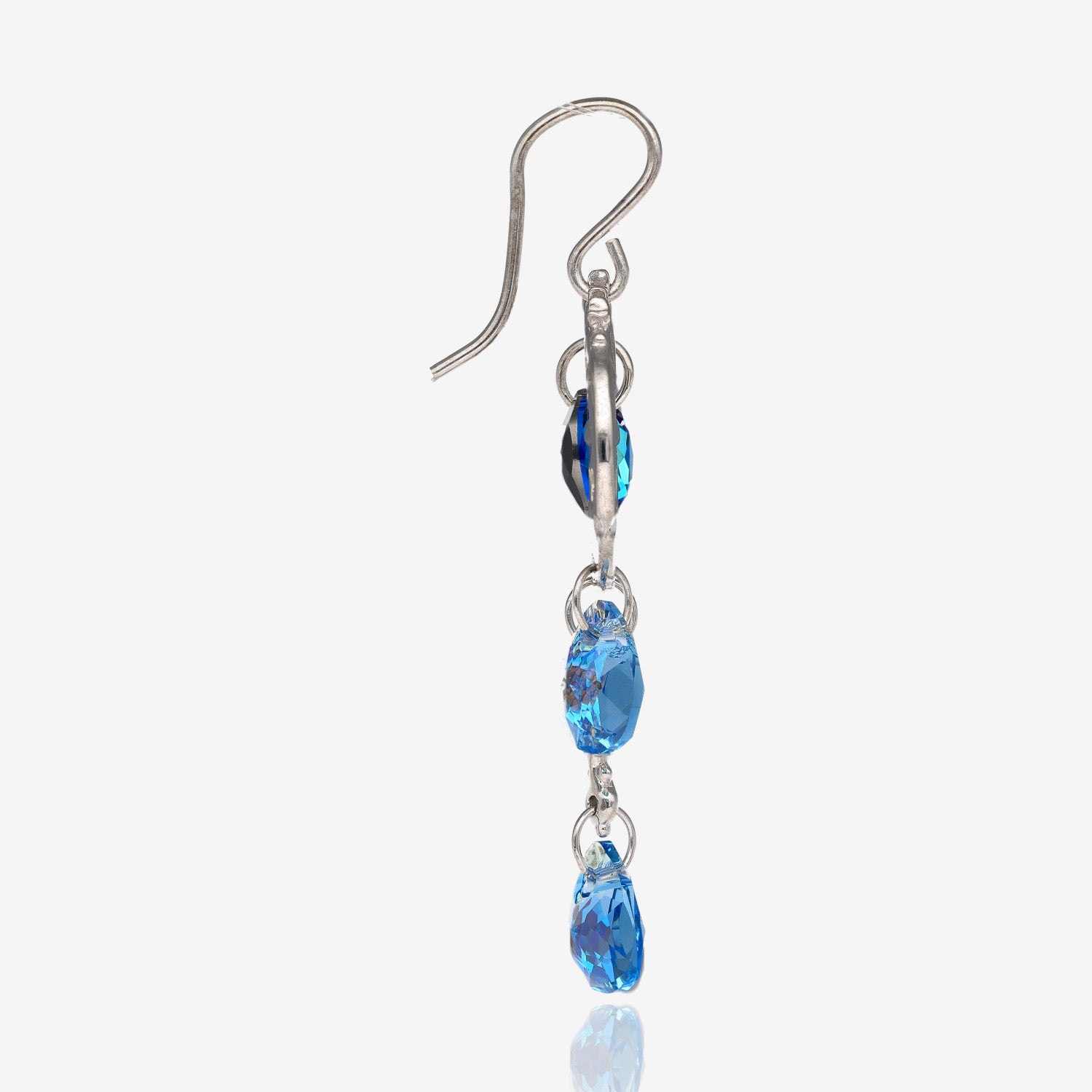 Side view of 1 silver earring shaped like a crescent moon with a dark blue circle-shaped gem bead in the center of the crescent, a heart shaped charm on the bottom of the earring located towards the point of the crescent, and 2 light blue tear-shaped gem beads on the bottom of the earring.