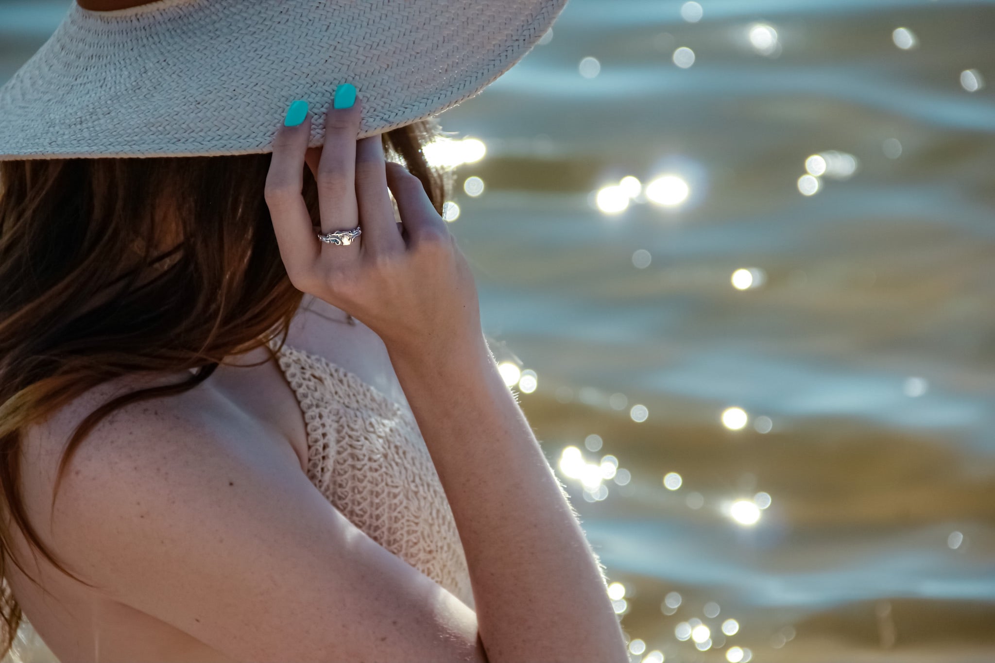 Woman wears a silver ring with a raised, polished michigan shape visible. Woman has a hat on and is standing near a lake