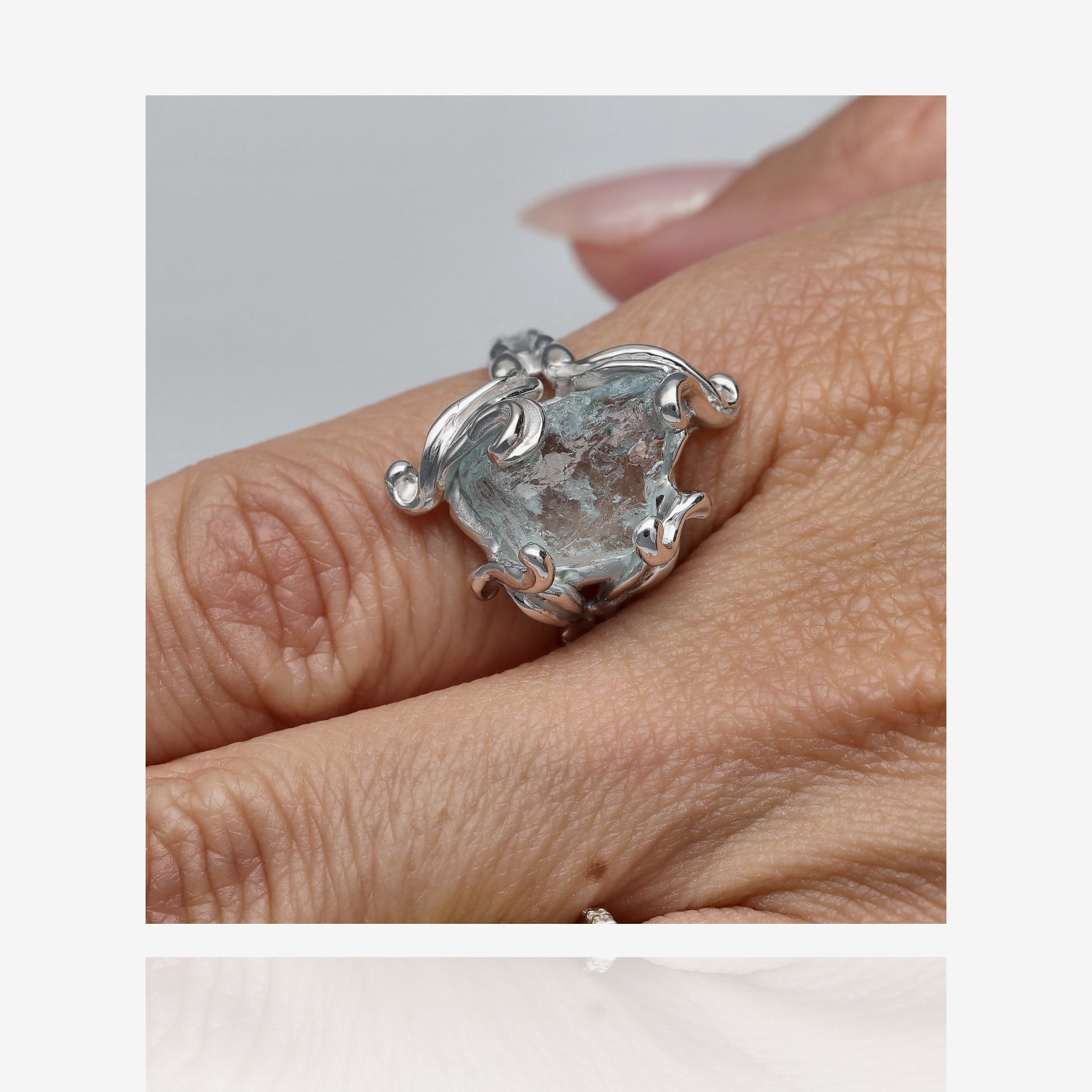 Silver ring on hand with raw gem. Pale blue aquamarine approximately three quarters of an inch long