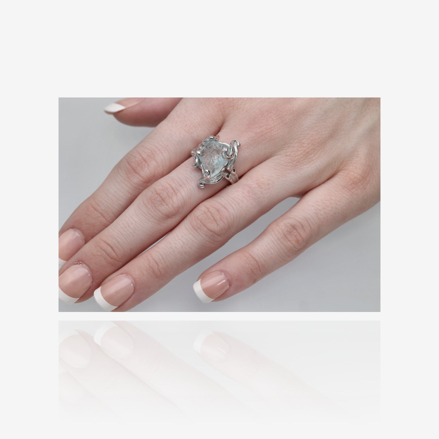 Photo of pale blue gem ring on hand. Gemstone is unfaceted aquamarine set in silver swirls