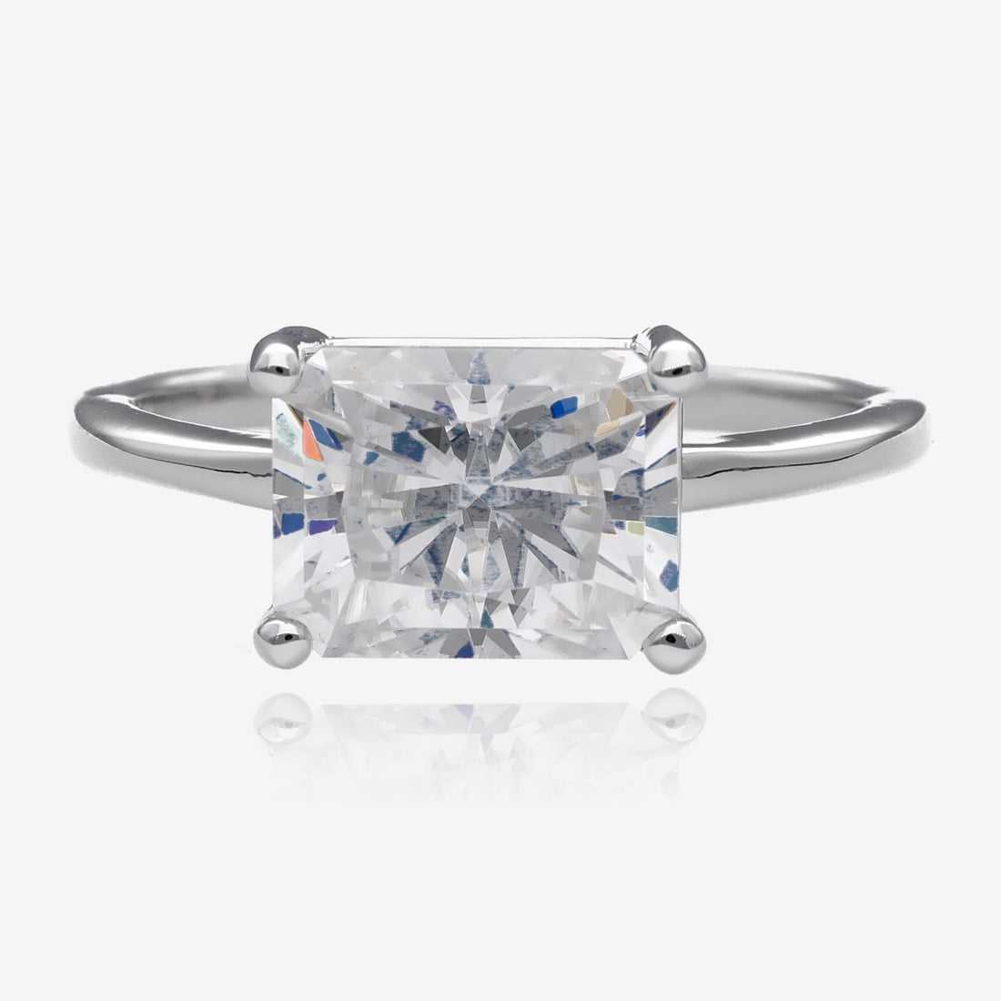 Large radiant rectangular cut white moissanite is set east west in a simple slender white gold ring with four prongs