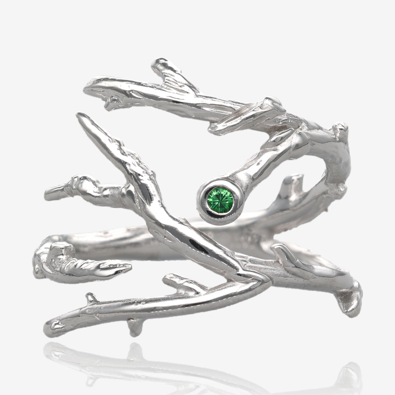 Twigs and branches form a ring that is adjustable, open on top and approximately 3/4” wide. A single small green gemstone is set into a bezel at the tip of one branch