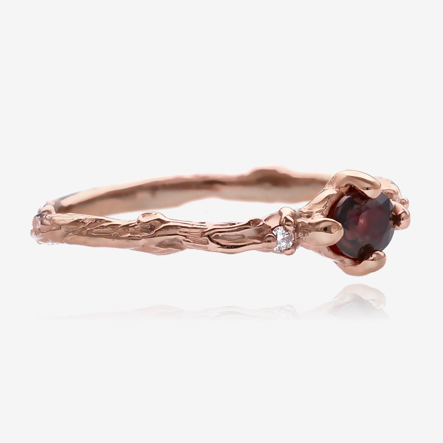 Side view of twig ring. Plum purple faceted oval sapphire is set lengthwise in a slender, bark textured rose gold band with a small diamond on each side