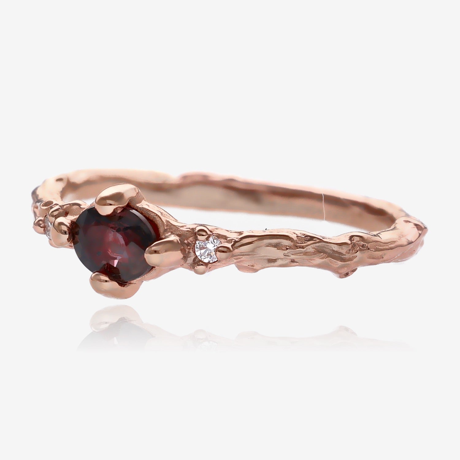 Side view of twig ring. Plum purple faceted oval sapphire is set lengthwise in a slender, bark textured rose gold band with a small diamond on each side