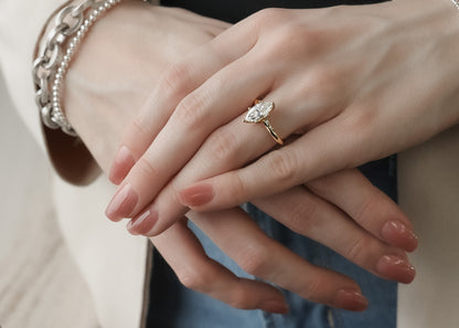 Woman’s hand wearing bracelets and a yellow gold marquise diamond engagement ring. Diamond is one and quarter carat and set lengthwise 