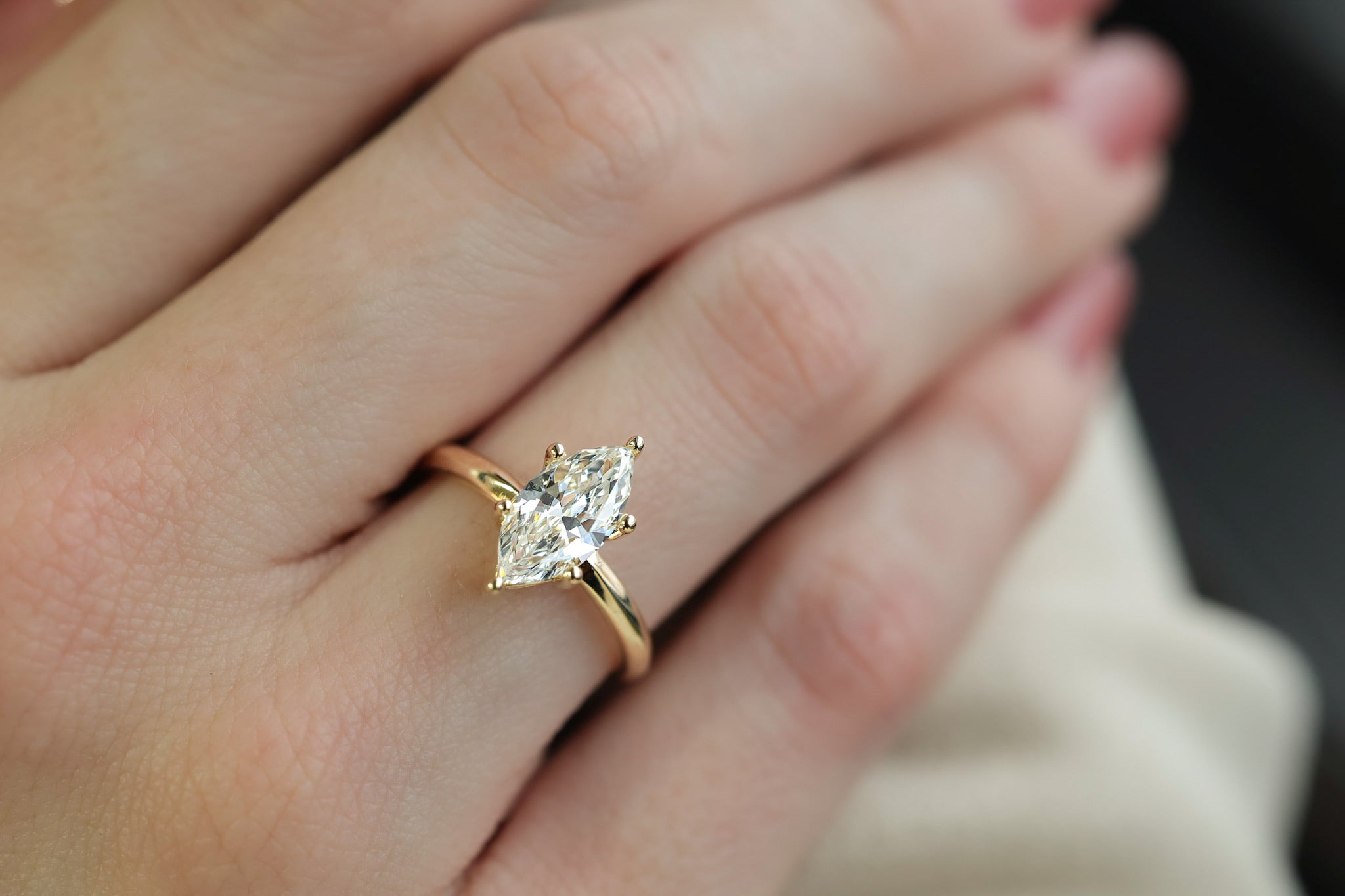 Woman’s hand wearing a yellow gold marquise diamond engagement ring. Diamond is one and quarter carat and set lengthwise 