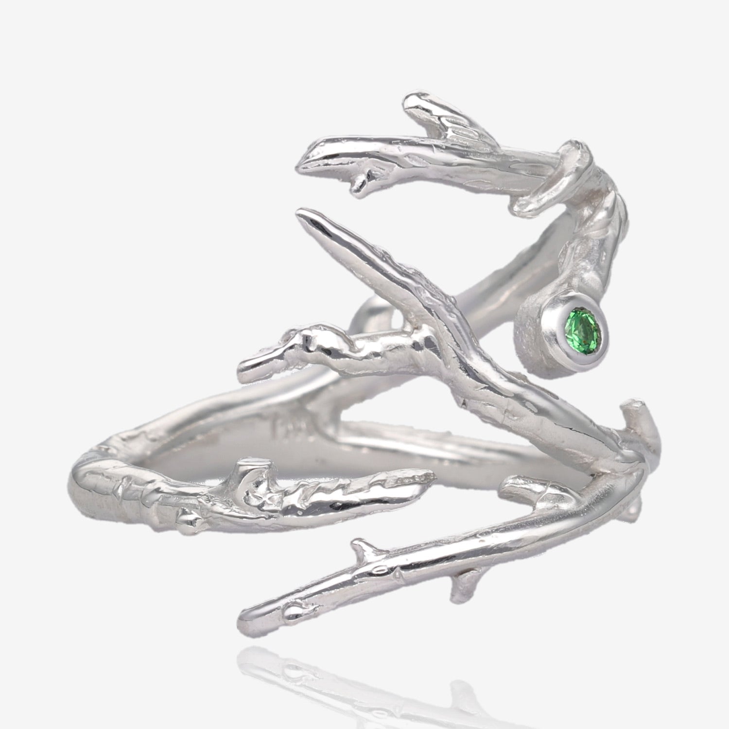 Side view of ring showing multiple tree branches that connect on the bottom to form the band. A small green gem is visible on top of the design, small branches point in different directions 