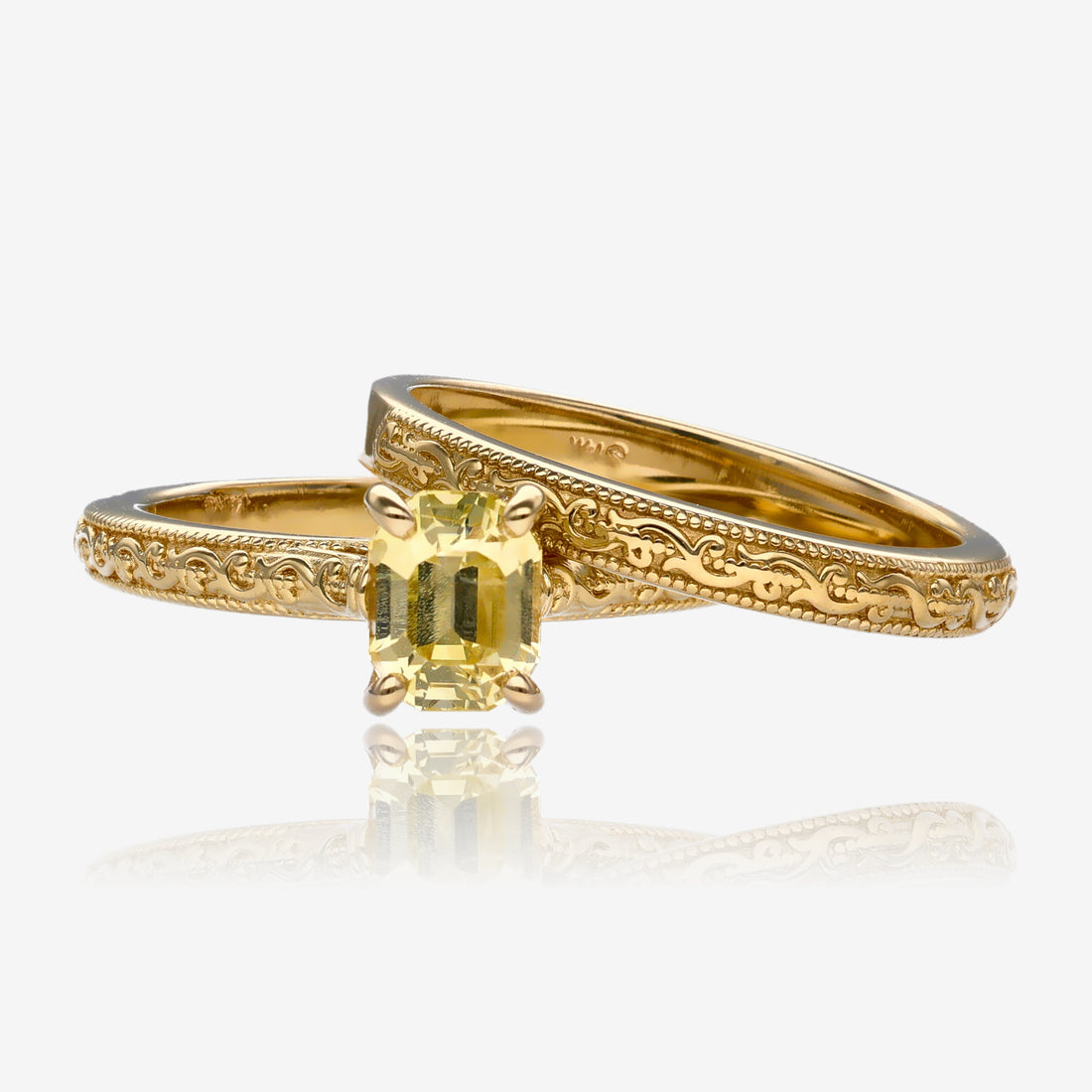 Yellow gold engagement ring, set with vintage detailing and emerald cut sapphire in a pale, lemon, yellow. Stone is set with four prongs, each band measures approximately 2 mm thick.