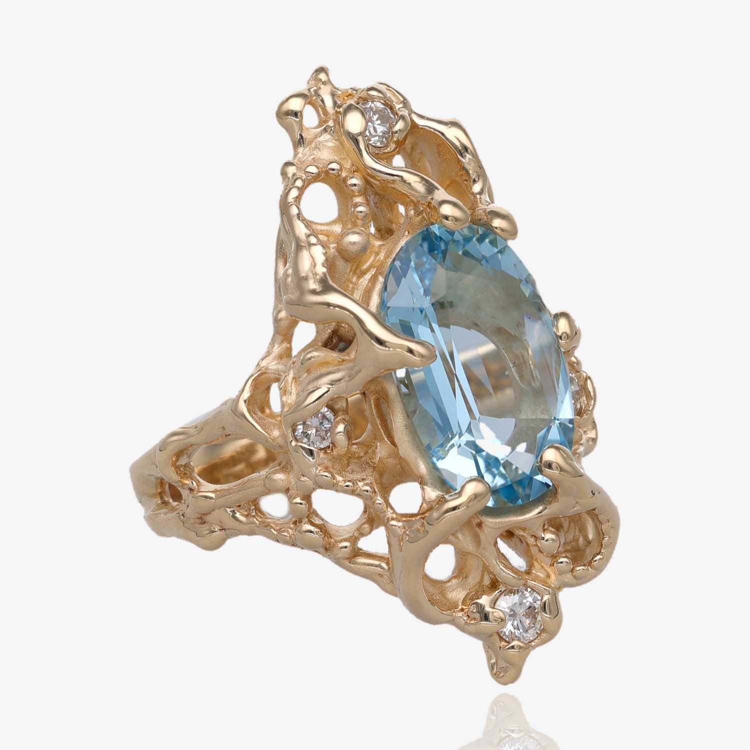 Side view of Yellow gold ring approximately one inch long. Design holds a light blue oval shaped gemstone that is held in by six prongs. The design of the ring is abstract and asymmetrical with raised gold dots and four small diamonds