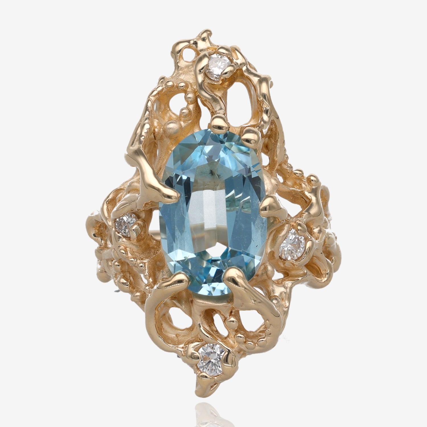 Yellow gold ring approximately one inch long on top.it is holding a light blue oval shaped gemstone that is held in by six prongs. The design of the ring is swirling, abstract and asymmetrical with raised gold dots and four small diamonds