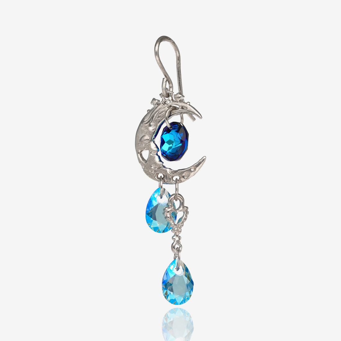 Front view of 1 silver earring shaped like a crescent moon with a dark blue circle-shaped gem bead in the center of the crescent, a heart shaped charm on the bottom of the earring located towards the point of the crescent, and 2 light blue tear-shaped gem beads on the bottom of the earring.