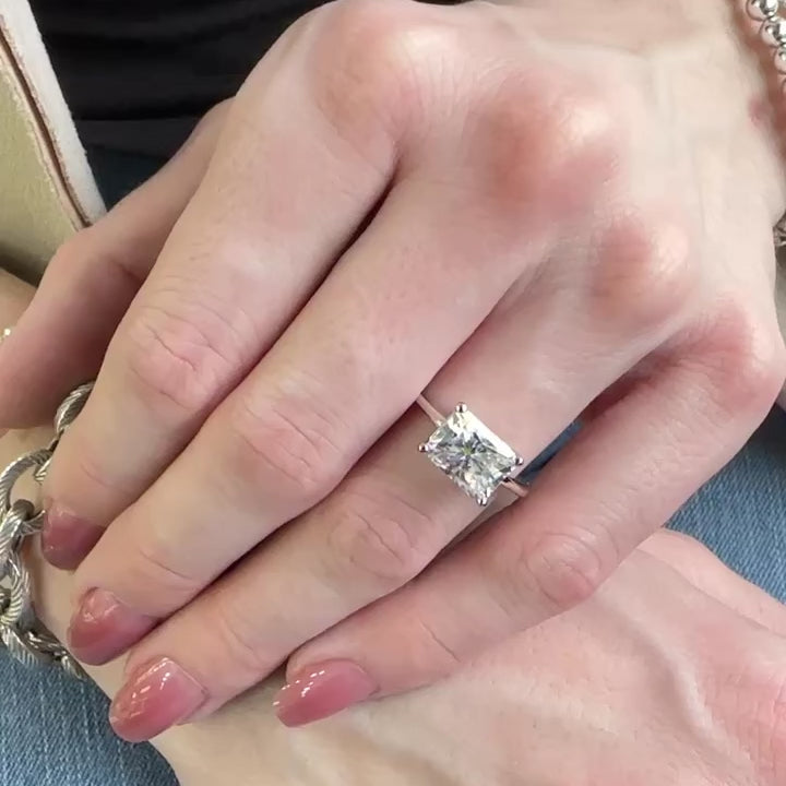 Woman’s hand wearing a solitaire white moissanite rectangular radiant cut in a white gold band