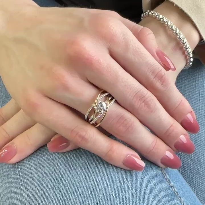 A woman’s hand wears an open work, two-tone gold ring with a round diamond center and several dozen small diamond accents in three rows