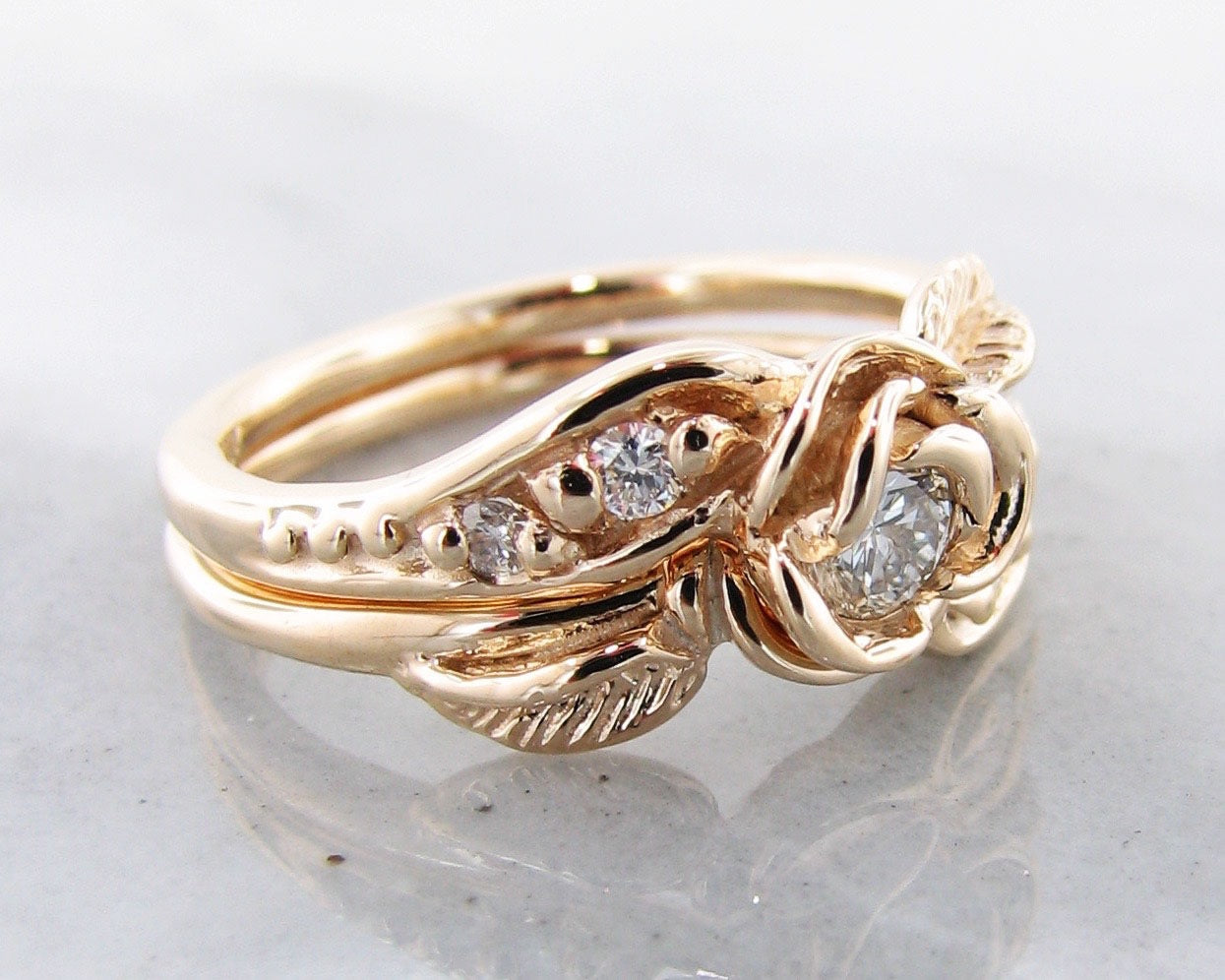 Side view of yellow gold wedding set with a rose bloom center. The rose is made up of five petals that curve around a diamond. A leaf curves around the band of the engagement ring, and the wedding band has small diamonds set low into the design