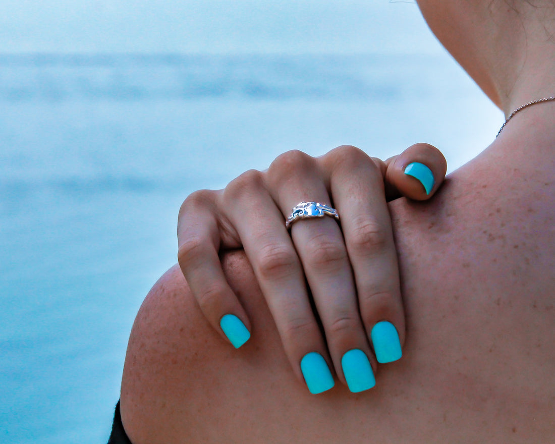 Woman wears a silver ring with a raised, polished michigan shape visible. in the background is theLake MIchigan coastline