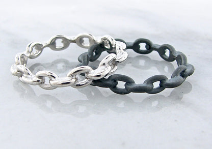 image shows two silver bands made of fused chain links. one band is high polished silver finish, the other is matte black